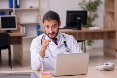 Genç erkek doktor ofiste oturuyor.