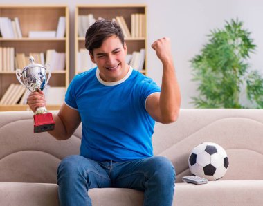 Evdeki kanepede oturup futbol izleyen bir adam.