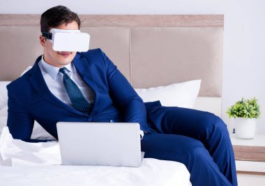 Yatak odasında sanal gerçeklik kulaklığı takan bir iş adamı.