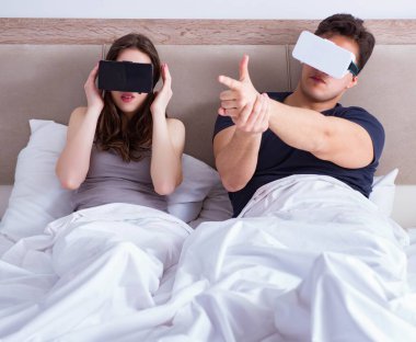 Yatakta sanal gerçeklik gözlüklü eş ve koca.