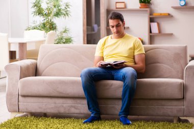 Evde kitap okuyan genç bir erkek öğrenci.