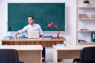 Genç erkek öğretmen yeşil panonun önünde.