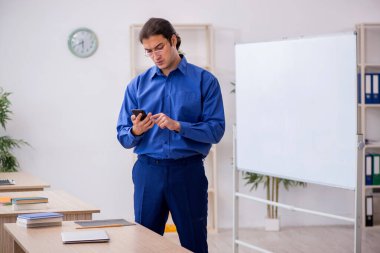 Genç erkek öğretmen ders sırasında elinde akıllı telefon tutuyor.
