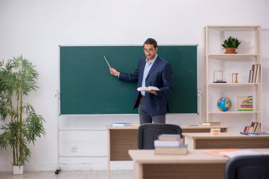 Genç erkek öğretmen yeşil panonun önünde.