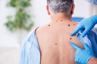 Yaşlı adam genç erkek doktor dermatoloğu ziyaret ediyor.