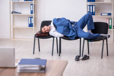 Genç bir erkek çalışan ofiste koltuklarda uyuyor.