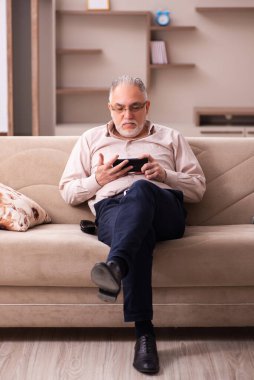 Yaşlı adam evdeki kanepede oturuyor.
