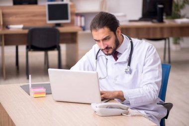 Genç erkek doktor ofiste oturuyor.