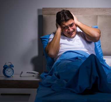 Genç adam yatakta gürültüden boğuşuyor.