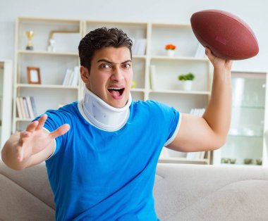 Boynu yaralanmış bir adam evde Amerikan futbolu seyrediyor.