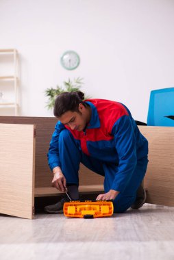 Genç erkek müteahhit ofiste mobilya tamir ediyor.