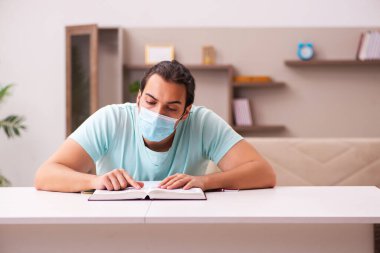 Genç erkek öğrenci salgın sırasında evde çalışıyor.