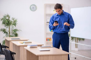 Genç erkek öğretmen ders sırasında elinde akıllı telefon tutuyor.