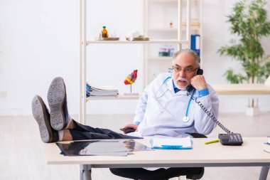 Yaşlı erkek doktor klinikte telefonla konuşuyor.