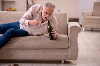 Yaşlı adam evde alkol içiyor.