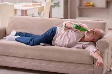 Yaşlı adam evde alkol içiyor.