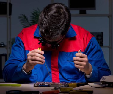 Bilgisayar uzmanı gece geç saatlerde bilgisayarı tamir ediyor.