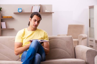 Evde kitap okuyan genç bir erkek öğrenci.