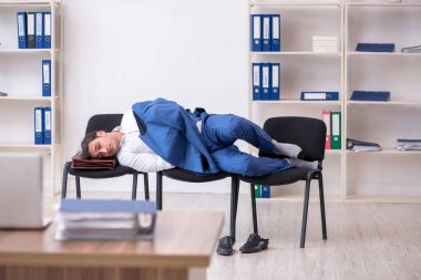 Genç bir erkek çalışan ofiste koltuklarda uyuyor.