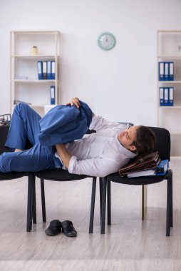 Genç bir erkek çalışan ofiste koltuklarda uyuyor.