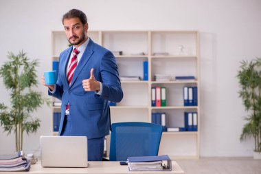 Genç erkek çalışan işyerinde kahve içiyor.