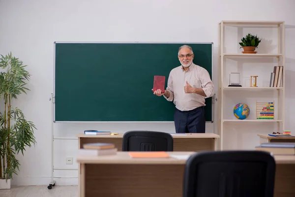 Old male teacher in front of blackboard