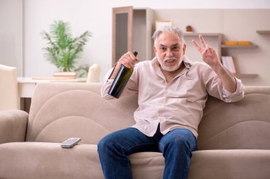 Yaşlı adam evde alkol içiyor.