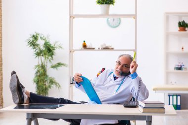 Yaşlı erkek doktor klinikte telefonla konuşuyor.