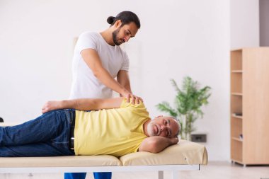 Yaşlı erkek hasta, genç erkek doktor masörünü ziyaret ediyor.