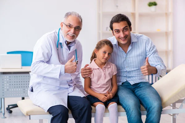 Small girl with her father visiting old male doctor