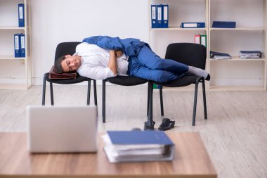 Genç bir erkek çalışan ofiste koltuklarda uyuyor.