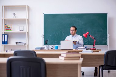 Genç erkek öğretmen yeşil panonun önünde.