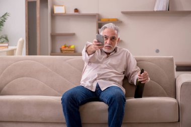 Yaşlı adam evde alkol içiyor.