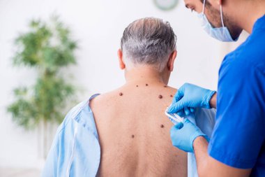 Yaşlı adam genç erkek doktor dermatoloğu ziyaret ediyor.