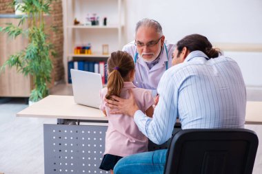 Babasıyla küçük bir kız yaşlı erkek doktoru ziyaret ediyor.