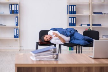 Genç bir erkek çalışan ofiste koltuklarda uyuyor.