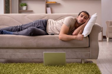 Evdeki kanepede yatan genç adam.