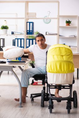 İş yerinde yeni doğan bebeğe bakan genç bir erkek işçi.