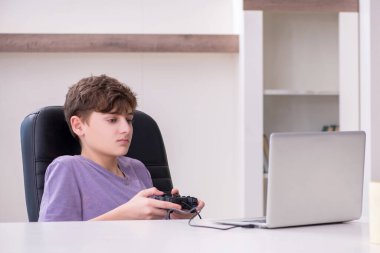 Okullu çocuk evde bilgisayar oyunu oynuyor.