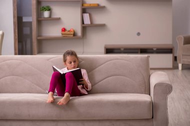 Evde kitap okuyan küçük bir kız.
