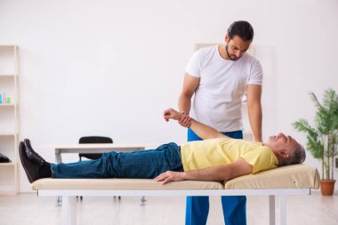 Yaşlı erkek hasta, genç erkek doktor masörünü ziyaret ediyor.