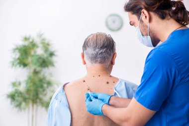 Yaşlı adam genç erkek doktor dermatoloğu ziyaret ediyor.