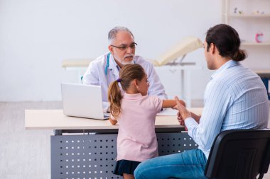 Babasıyla küçük bir kız yaşlı erkek doktoru ziyaret ediyor.