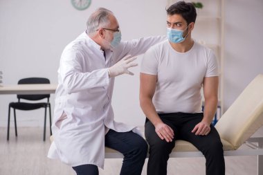 Genç erkek hasta yaşlı erkek doktoru aşıyla ziyaret ediyor.