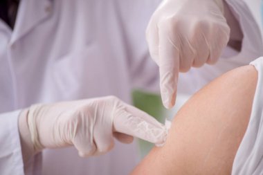 Genç erkek hasta yaşlı erkek doktoru aşıyla ziyaret ediyor.