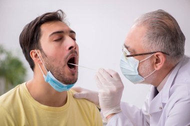 Genç erkek hasta yaşlı doktor otorhinolaryngologis 'i ziyaret ediyor.