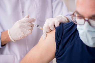 Yaşlı bir erkek hasta aşıyla genç bir doktoru ziyaret ediyor.