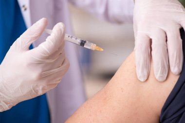 Yaşlı adam covid-19 aşı konseptinde genç doktoru ziyaret ediyor.