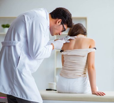 Doktor kadın hastanın derisini muayene ediyor.