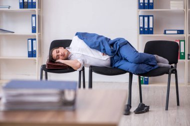 Genç bir erkek çalışan ofiste koltuklarda uyuyor.